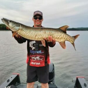 Jeremy wearing dark sunglasses, his ball cap and sponsor shirt holding a good sized "toothy gator" at shoulder height.