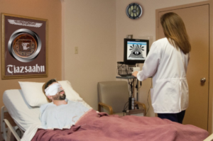 Ichabode lying in a hospital bed with bandages on his head covering his eyes in a room with an attending nurse. There are pictures on the walls displaying some of the ancient symbols as described previously.