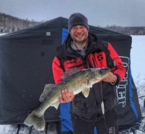 Jeremy holding a large fish in front of his ice hut.