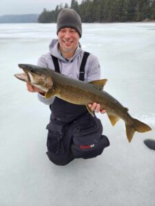 Jeremy kneeling on the ice while holding a record sized lake trout.