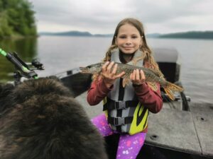 A young girl (Autumn) wearing a life jacket in a boat holding her fish that she caught.